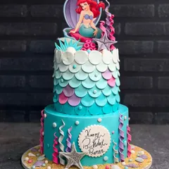 Let's plan an oceanic adventure with a custom mermaid cake. This two-tiered creation features beautiful teal and purple scales, an Ariel topper, and handcrafted sea elements, perfect for a magical under-the-sea birthday party.