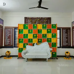 A vibrant and traditional backdrop perfect for a Haldi or baby shower ceremony. This setup uses a checkerboard pattern of green cloth with orange and yellow marigold flower strings.