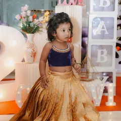 This little client is wearing a custom designer kids' lehenga choli. The outfit pairs a rich navy blue velvet top with a beautifully pleated golden silk brocade skirt, creating a stunning traditional look for her birthday celebration.