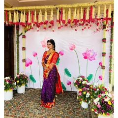 A full-length shot showcasing the entire look against the beautiful floral decor. The rich colors of her saree are enhanced by the classic makeup and simple, elegant hairstyle.