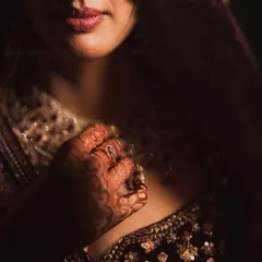 An artistic close-up focusing on the bride's lips and the intricate henna on her hand, capturing the sensual details of her look.