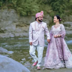 A royal walk by the riverside. The couple's elegant ethnic wear looks stunning against the rugged, natural backdrop of the river and green hills.