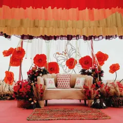 A closer look at the vibrant Mehendi stage, featuring bold red paper flowers, a wireframe butterfly motif, and layered, colorful ceiling drapes.