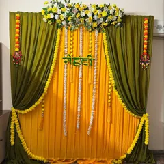 A beautiful Mehendi backdrop with olive and yellow drapes. The decor is adorned with marigold and jasmine flower strings, creating a classic and festive look.