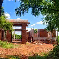 The "Elephants by the Lake" residence under construction, framed by trees. The design uses exposed brick and creates large openings to connect the inhabitants with the natural beauty of the site.