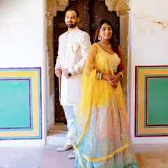This is how you coordinate without being too matchy. The groom's elegant ivory sherwani perfectly complements the bride's vibrant multi-colored lehenga, creating a balanced and visually stunning look for their pre-wedding shoot.