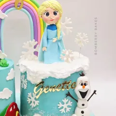 This magical cake for twins features two distinct themes, Frozen and Cars, connected by a rainbow. It showcases multiple fondant toppers, including a hand-sculpted Elsa, Olaf, and a personalized car.