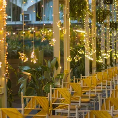 An evening view of our venue, where rows of chairs with yellow sashes are illuminated by cascading fairy lights, creating a warm and enchanting atmosphere for a ceremony or reception.