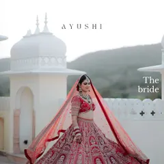 A majestic portrait of the bride, her red lehenga spread out, with the beautiful architecture of the venue creating a regal and expansive backdrop.