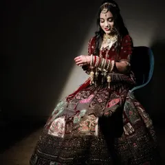 A serene portrait of the bride seated, captured with artistic spotlighting. She is admiring her hands, adorned with bangles and kaleeras, in a quiet moment of reflection.
