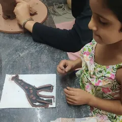 A young artist works on her clay enhanced silhouette. This activity encourages children to think about what makes them unique while exploring different textures and shapes with hand building techniques.