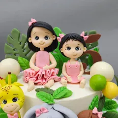 A close-up of the adorable, custom-made sister figurines for a jungle-themed birthday cake.