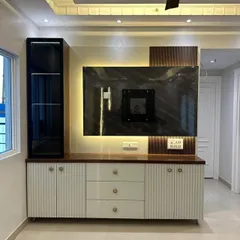 A contemporary TV and entertainment unit featuring a mix of materials. The design includes fluted white cabinets, a dark wood countertop, and a marble-patterned back panel with ambient lighting.