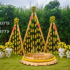 A modern and geometric Haldi backdrop. This outdoor setup uses triangular frames with marigold strings and large decorative vases, offering a contemporary twist on traditional decor.