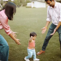 A baby's first steps towards her parents in a green park. Our outdoor lifestyle sessions are perfect for capturing these major family milestones naturally.
