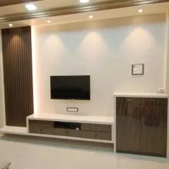 A simple yet elegant TV unit design. The combination of dark wood fluting, a clean white console, and warm spotlights creates a balanced and modern look for the living room.