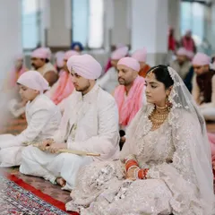 A serene moment from a Sikh wedding ceremony, or Anand Karaj. The soft color palette and the couple's calm demeanor reflect the peaceful and spiritual nature of the vows.