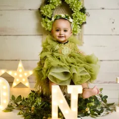 Turning one is a big deal. This setup uses marquee lights spelling "ONE" and a beautiful rustic theme to celebrate the milestone. The little girl's olive green dress and happy smile complete the perfect first birthday photo.