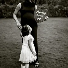 A beautiful black and white portrait of a mother and daughter. The little girl looks up at her mom with adoration as they hold a "Coming Soon" sign together.