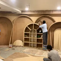 A team of carpenters works on an intricate plywood wall featuring a series of arches. This image captures the skill and precision involved in executing our custom designs.