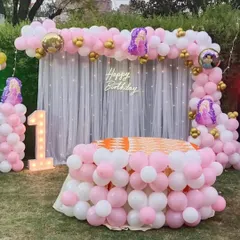 A princess-themed first birthday party set up on a lawn, with a full balloon arch and decorated table.