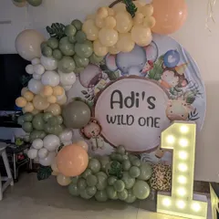 Celebrating a 'Wild One' first birthday with a trendy jungle-themed backdrop. This setup uses a gentle, earthy color palette of sage green and beige balloons, a personalized sign, and a large marquee number to mark the special milestone.