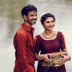 A happy, candid moment between the couple during their traditional pre-wedding shoot by the water. The makeup is natural and fresh, perfect for an outdoor, daytime setting.