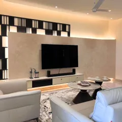 In this living room, the TV wall is a statement piece, featuring a soft textured finish and a bold geometric frame. The design is complemented by cove lighting and plush leather sofas, creating a space that feels both stylish and incredibly warm.
