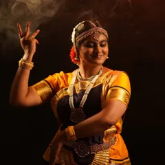 A close-up of a dancer in a traditional Bharatanatyam costume, highlighting the intricate temple jewelry, headpiece, and expressive hand gestures.