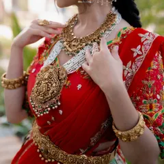 This shot is all about the jewelry. A close-up on the model's torso showcases an opulent antique temple jewelry set, including a large pendant necklace and waist belt, against a vibrant red bridal lehenga.