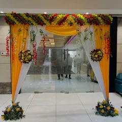 A bright and cheerful entrance gate for a party or function, decorated with yellow and white drapes and a mix of real and artificial flowers.