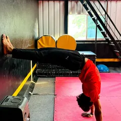 A student practices a wall-assisted handstand push-up, a fantastic exercise for building shoulder strength and core control.