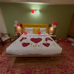 A beautiful and romantic bedroom decoration for a first night or anniversary. The bed is adorned with rose petals forming hearts and the letters 'P' and 'A', with balloons and petals on the floor.