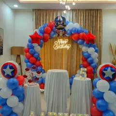 A Captain America themed birthday decoration with a red, white, and blue balloon arch, a 'Happy Birthday' neon sign, and Captain America's shield props.