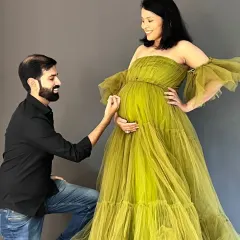 A tender moment between parents-to-be. Our olive green off-shoulder tulle gown adds a touch of soft elegance to this studio maternity session, perfectly complementing the partner's classic black shirt for a coordinated look.
