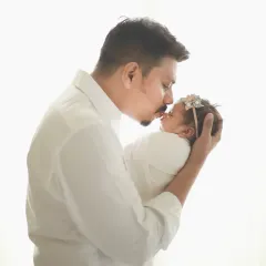A classic silhouette-style portrait of a father and his newborn. The high-key lighting creates a soft, dreamy effect, highlighting the delicate features of the baby and the loving embrace of her dad.