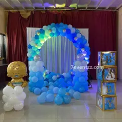 A blue and white themed baby shower or welcome baby boy decoration, featuring a circular balloon arch and 'BABY' blocks.