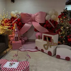 The complete setup for Anika's Christmas house party, featuring a festive backdrop with a giant pink bow, a custom train prop, and a beautifully decorated tree.