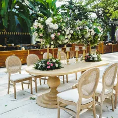 An elegant dining setup featuring a classic wooden table and tall floral centerpieces. The combination of white and pink flowers with lush greenery creates a timeless and romantic look.