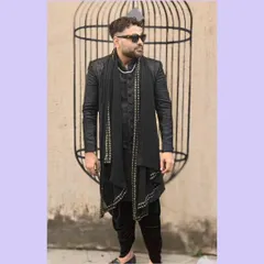 A full-length view of the black-on-black Indo-Western outfit. The asymmetrical cut and the embellished scarf create a look that is both traditional and fashion-forward.