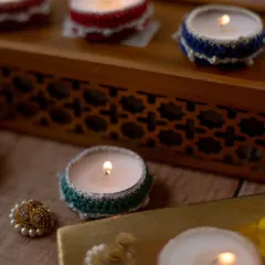 Our crochet tea light holders in various colors, shown lit in a cozy setting. These small 'diya jackets' are perfect for scattering around the house to create a warm, festive glow.