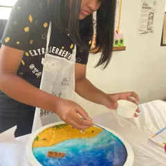 A student carefully places elements onto her resin beach art piece. This popular workshop teaches you how to create a beautiful ocean scene using resin, sand, and shells.