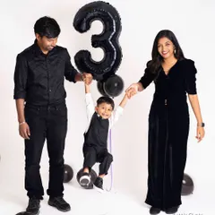 A playful family shot celebrating a third birthday. The parents swing their son, who is holding onto the number '3' balloon, creating a dynamic and joyful image.