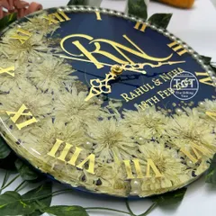 A close-up shot focusing on the intricate details of the preserved white flowers and the elegant clock hands over the couple's names.