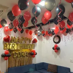 A living room decorated with red and black balloons on the ceiling, a gold fringe backdrop, and personalized name balloons.