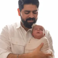 A father cradling his newborn daughter. My newborn sessions are calm and gentle, focusing on the safety of your baby while capturing these precious first moments.