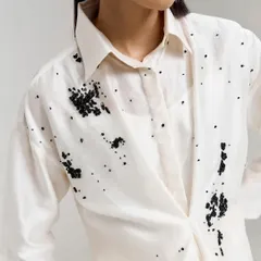 A close-up of the draped ivory shirt, showcasing the delicate black beaded embellishments that create the artistic splatter effect.