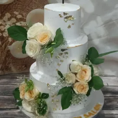 An elegant three-tiered wedding cake with a unique offset design. It's adorned with delicate fresh-looking sugar roses and baby's breath, with a touch of edible gold leaf for a hint of luxury.
