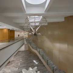 A grand staircase in a double-height lobby, anchored by a sculptural light fixture hanging from a skylight. Here, the staircase acts as a compositional focal point, organizing the space and inviting movement.