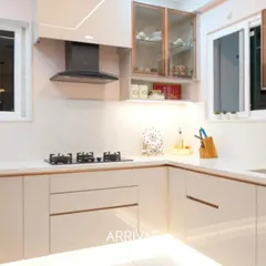 An elegant and bright L-shaped kitchen in a timeless beige finish. This design features a combination of solid and glass-front upper cabinets, sleek handleless drawers, and integrated under-cabinet lighting that creates a warm, inviting, and highly efficient workspace.